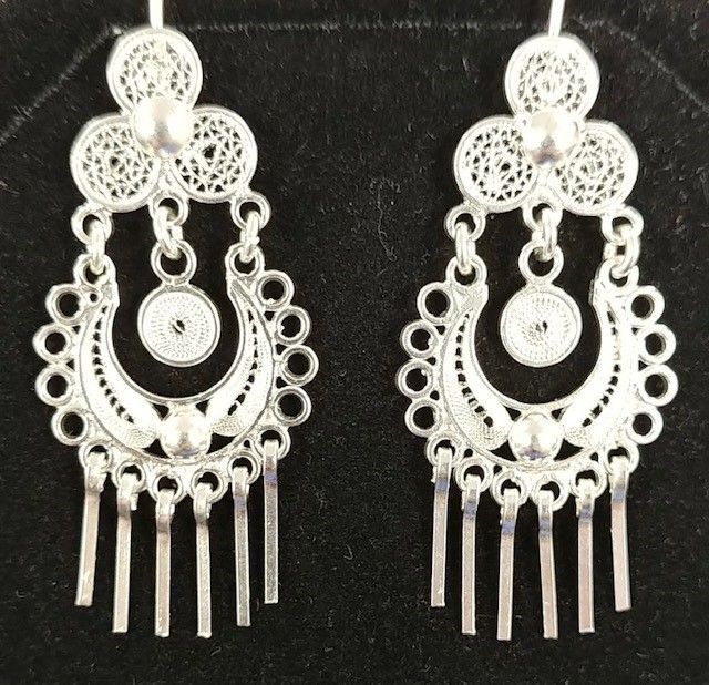 A pair of silver earrings are sitting on a black surface