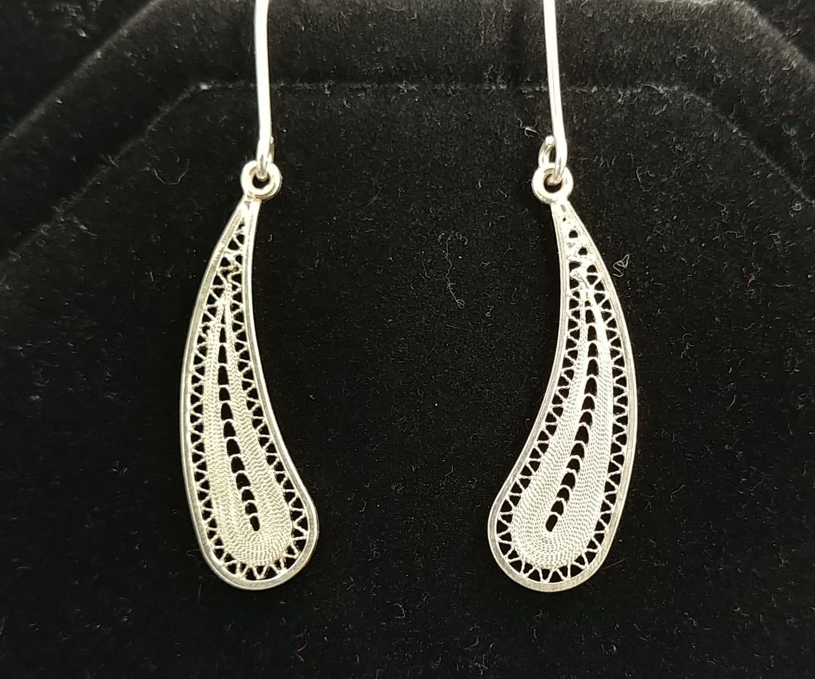 A pair of silver earrings are sitting on a black surface