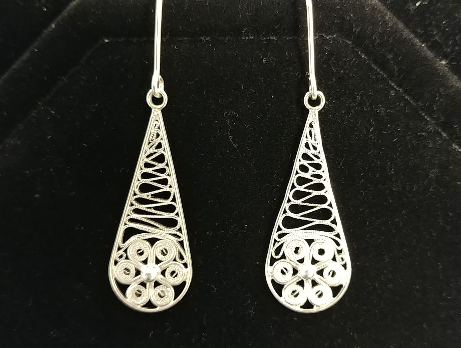 A pair of silver earrings are sitting on a black surface
