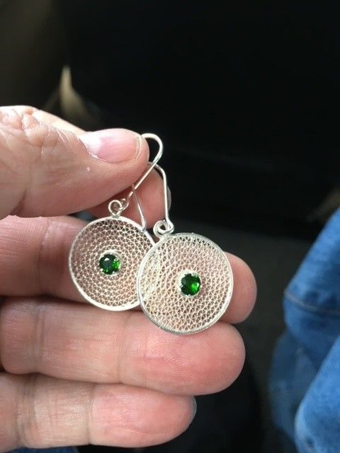 A person is holding a pair of silver earrings with green stones