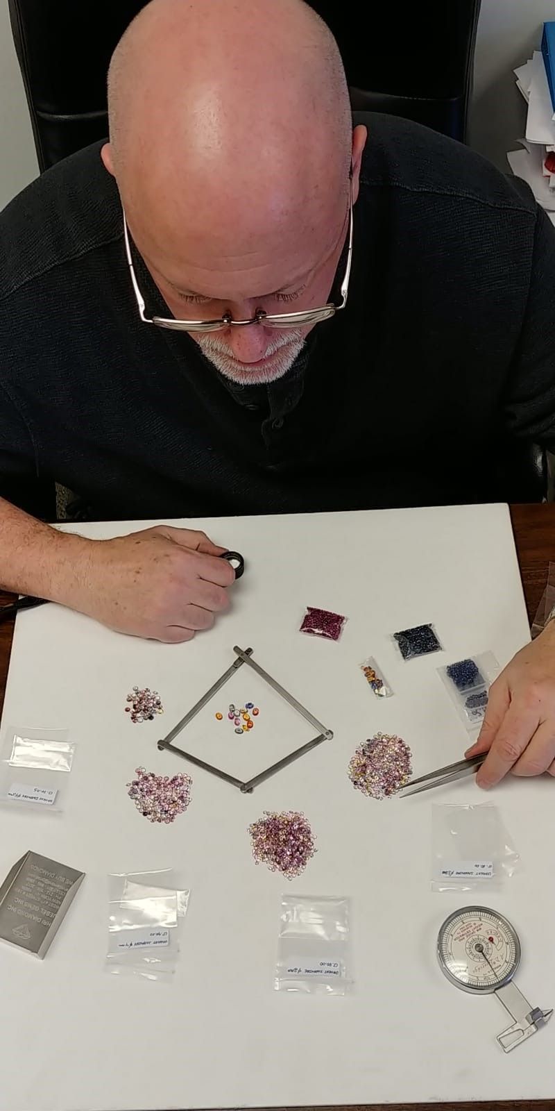 A bald man is sitting at a table with a bunch of jewelry on it.