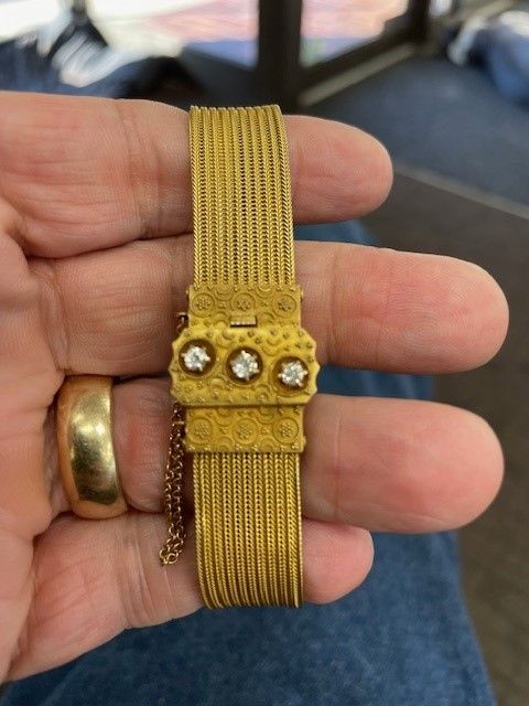A person is holding a gold bracelet with three diamonds on it