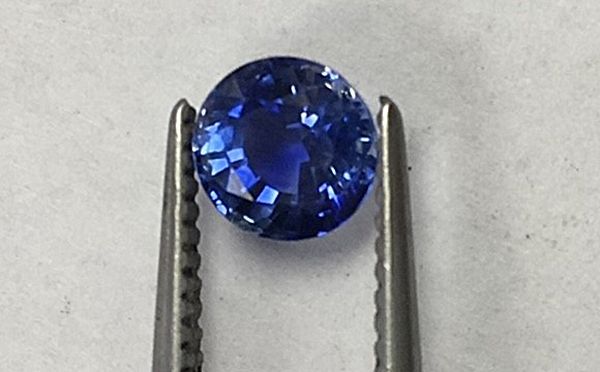 A blue sapphire is sitting on a pair of tweezers.