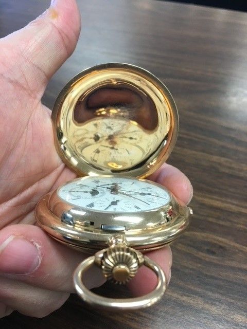 A person is holding a gold pocket watch in their hand