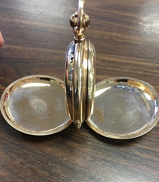 A gold pocket watch is open on a wooden table