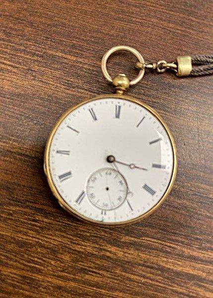 A gold pocket watch is sitting on a wooden table.