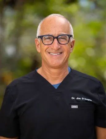 A man wearing glasses and a black scrub top is smiling for the camera.