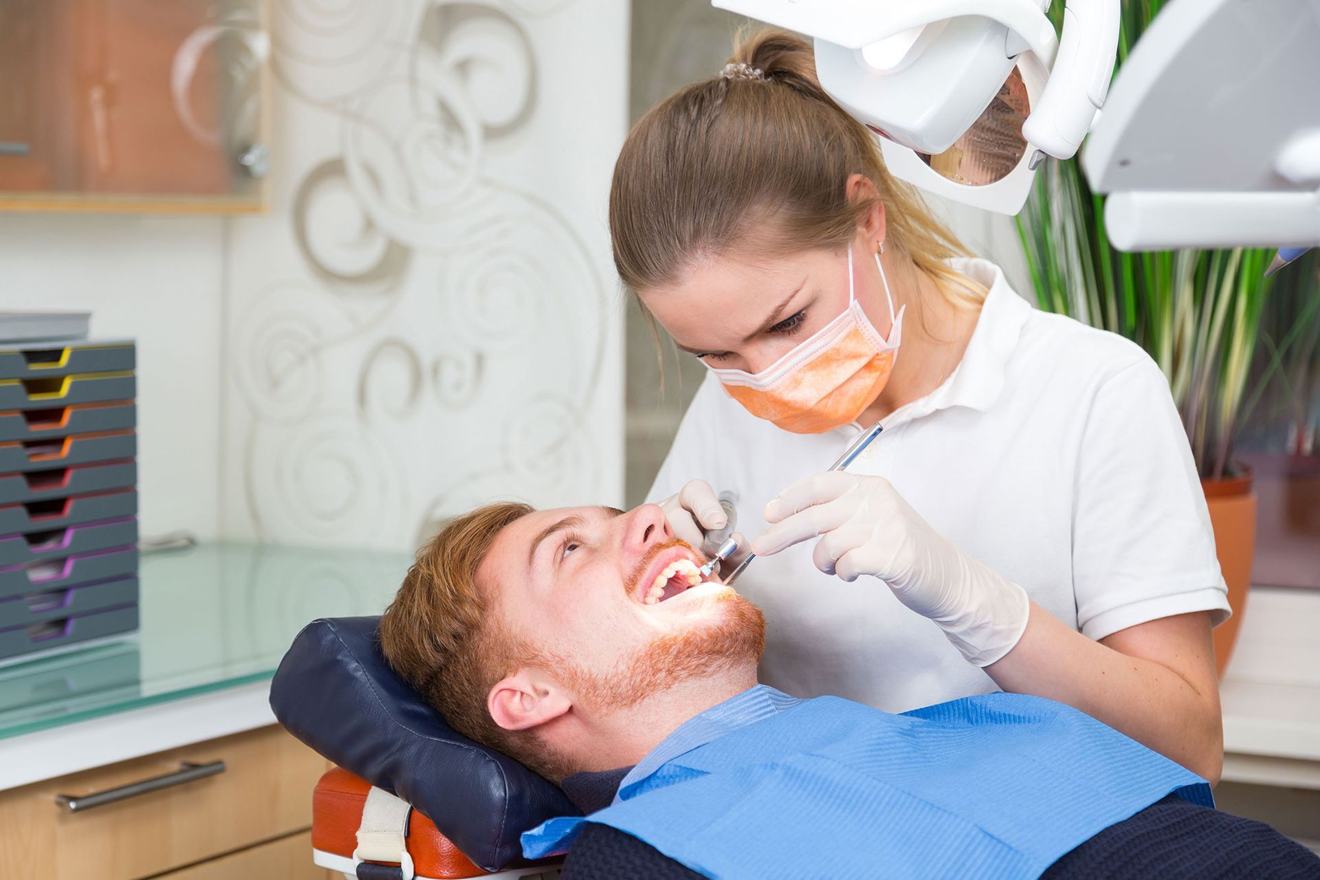 Dentist examining a patient's teeth. The patient is in a dental chair, the dentist is using tools.
