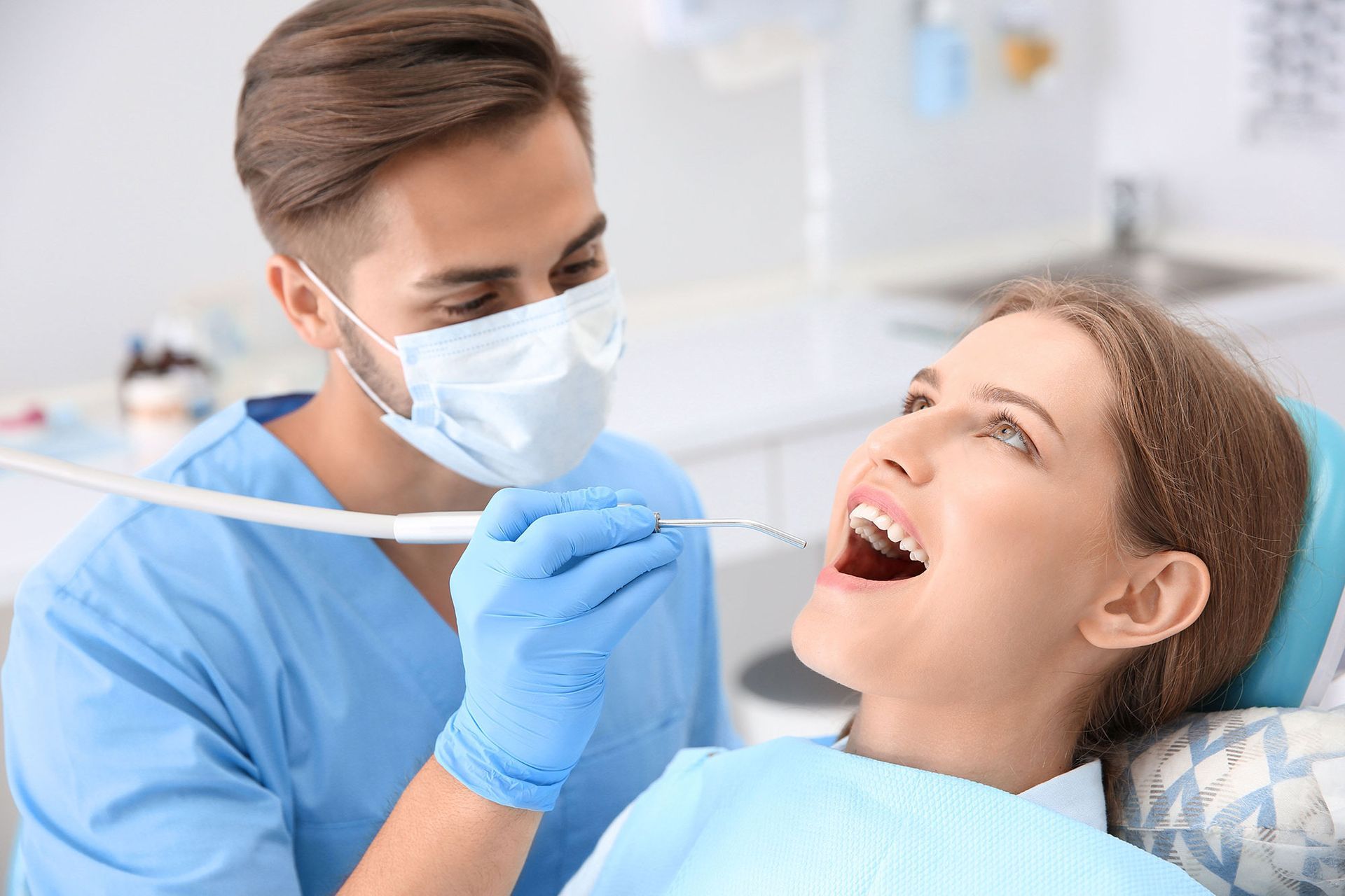 Dentist examining a woman's teeth in a dental office. The dentist wears a mask and gloves.