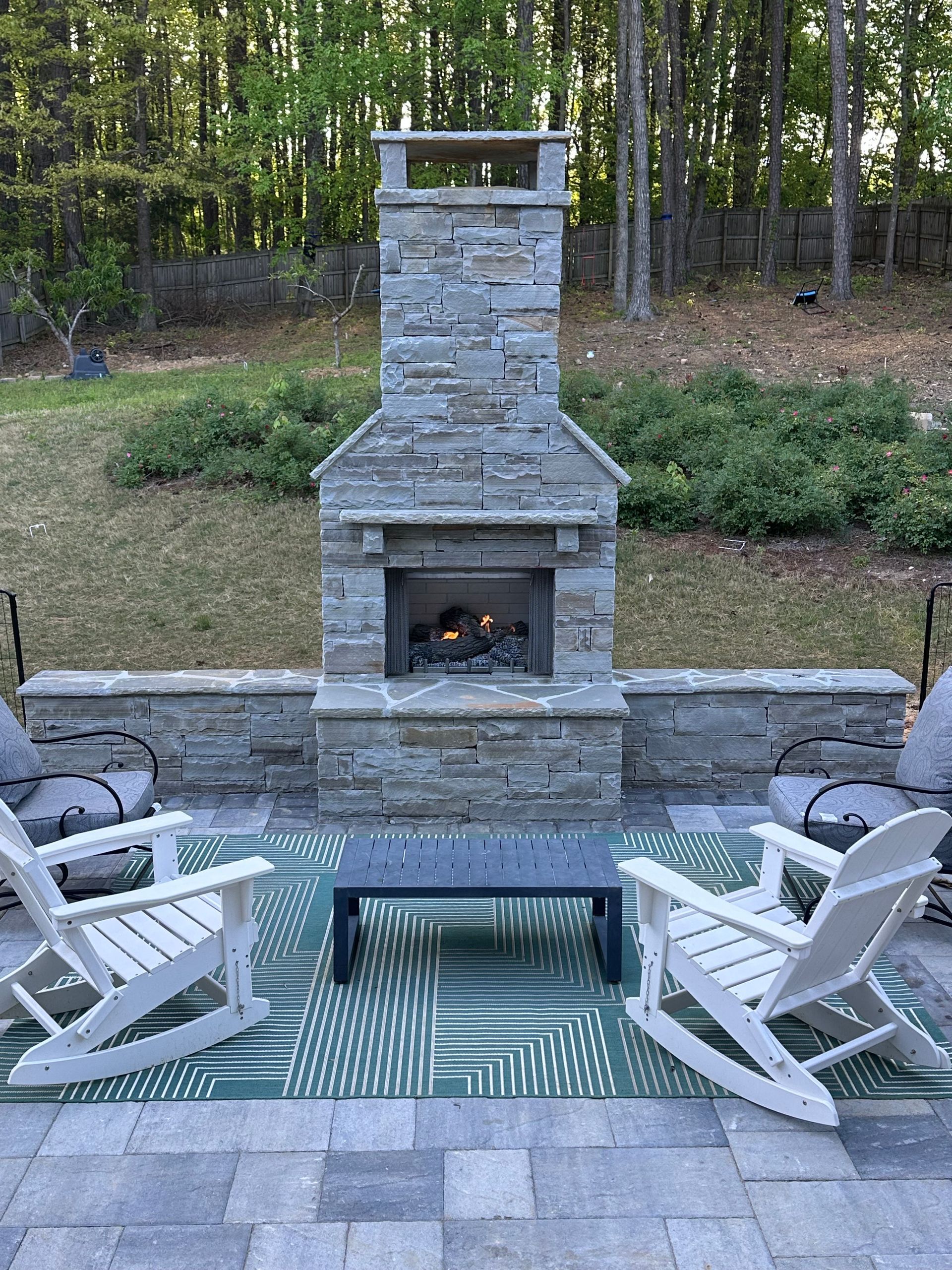 A patio with rocking chairs and a fireplace.