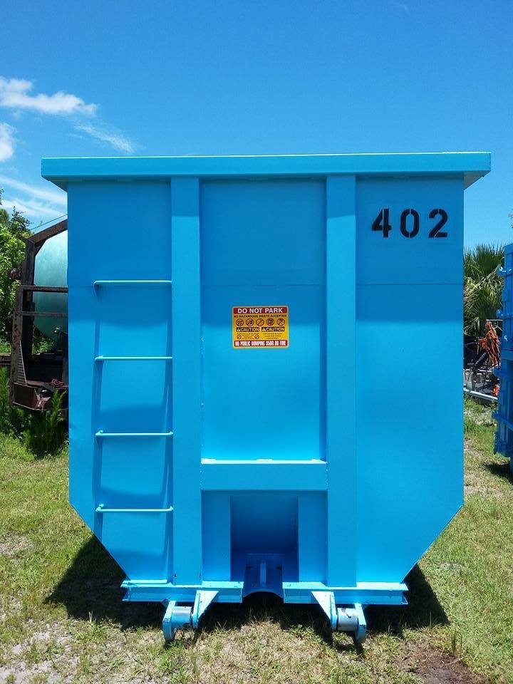 A blue dumpster with the number 402 on it is sitting in the grass.