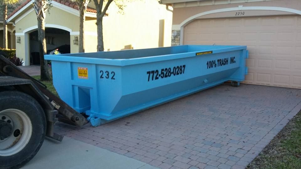 A blue dumpster is parked in front of a house