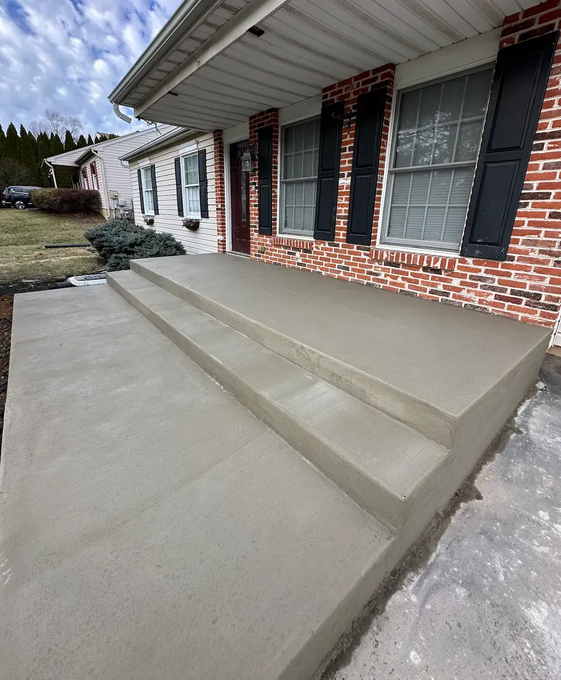Newly poured concrete porch and steps in front of a brick house with black shutters.