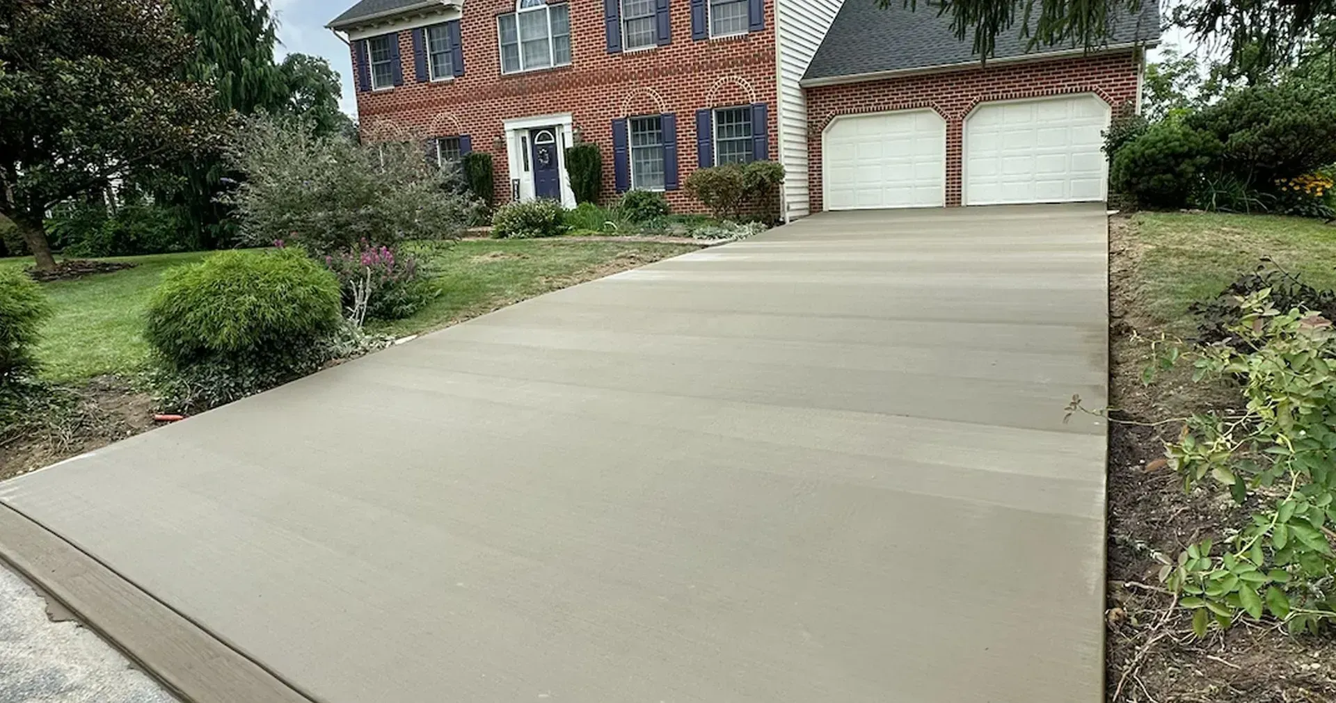 Wide concrete driveway leading up to a brick house with a two-car garage.