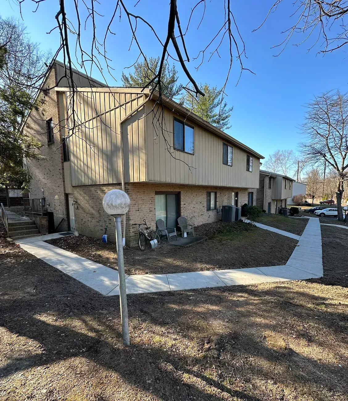 Two-story tan and brick townhomes on a sunny day. A concrete walkway leads to the front doors.