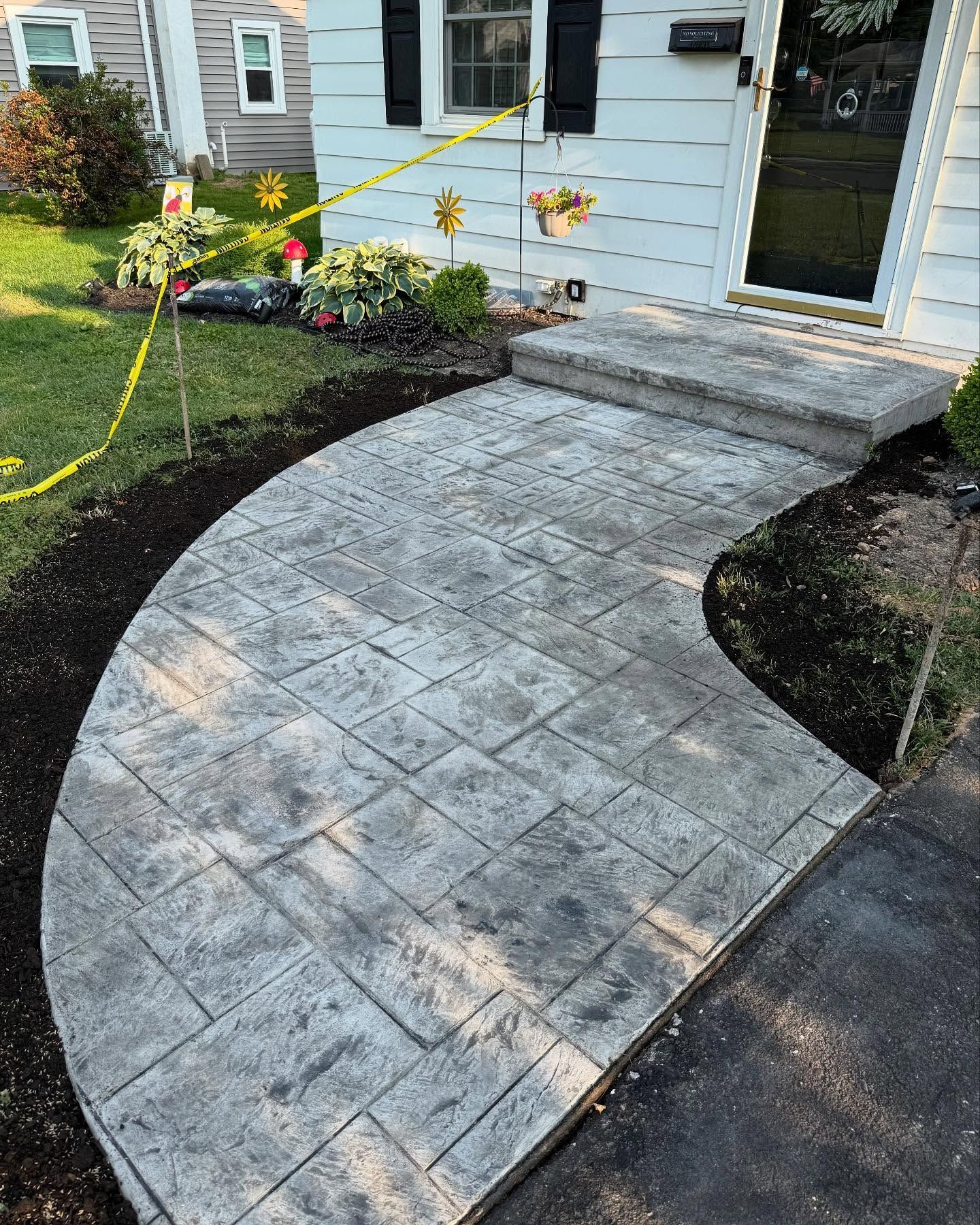 Curving concrete walkway with textured pattern leads to a home's front door and small porch steps.