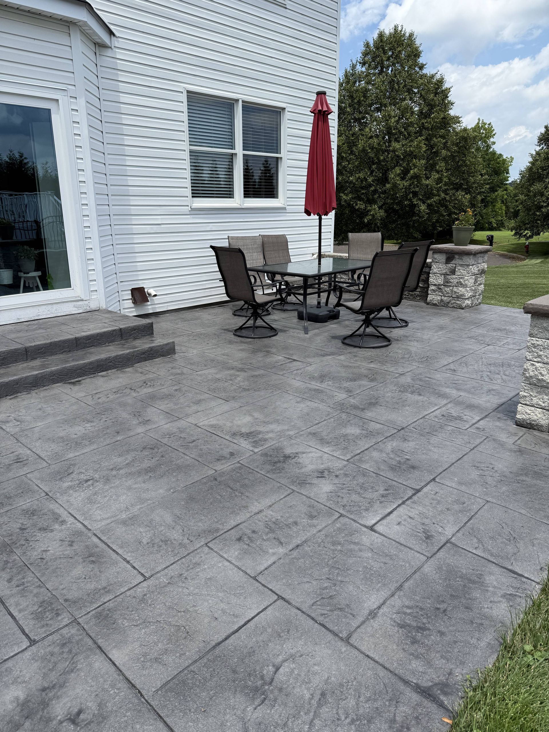 Outdoor patio with dark gray patterned concrete, seating, and a red umbrella.