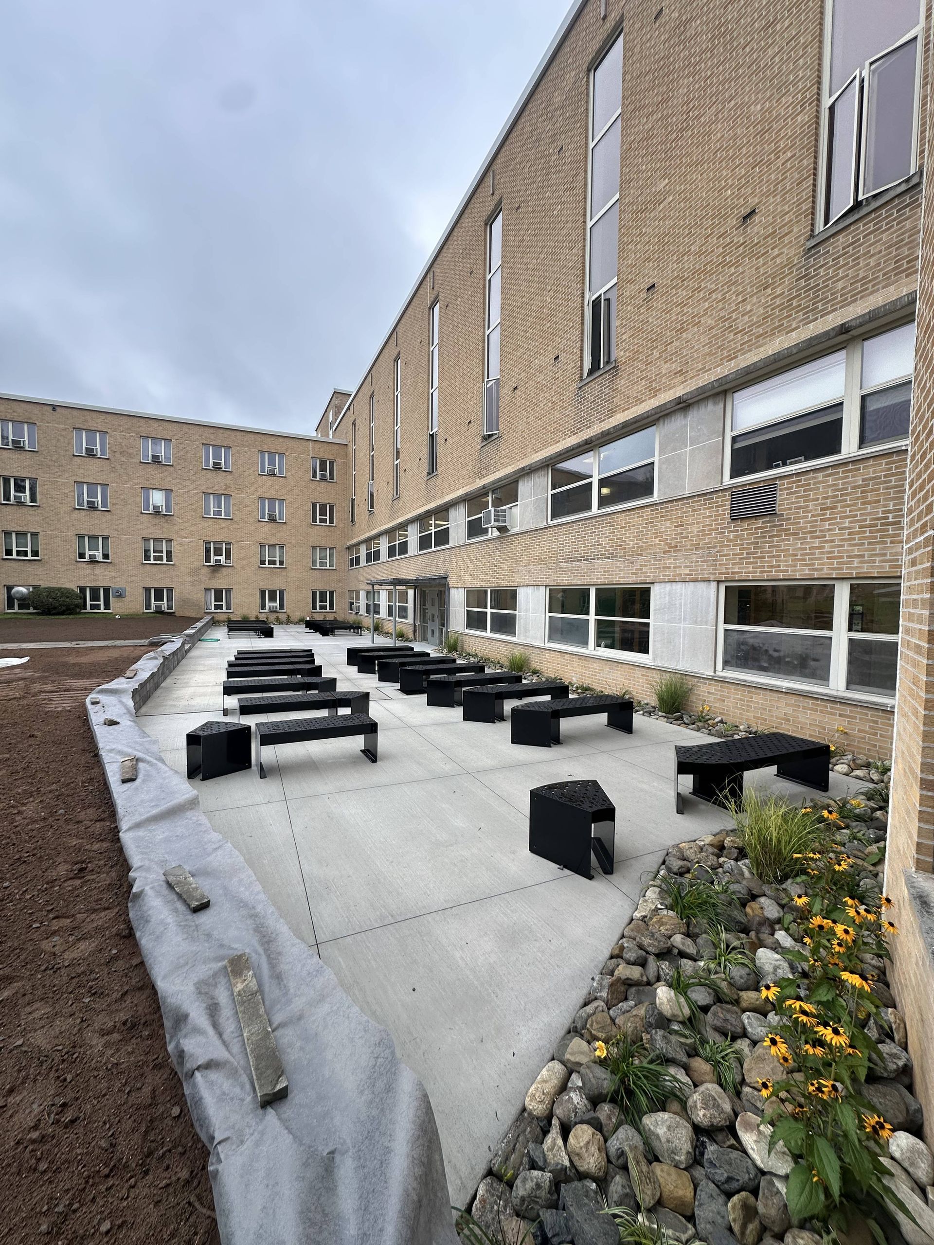 Outdoor patio with black benches, adjacent to a brick building, under an overcast sky.