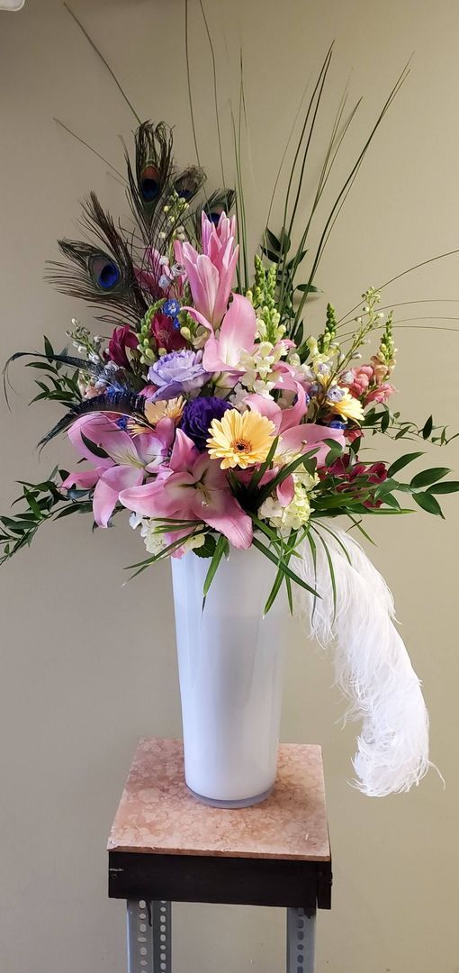 A vase filled with flowers and feathers is sitting on a table.