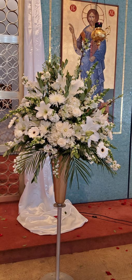 A vase filled with white flowers is in front of a picture of jesus.