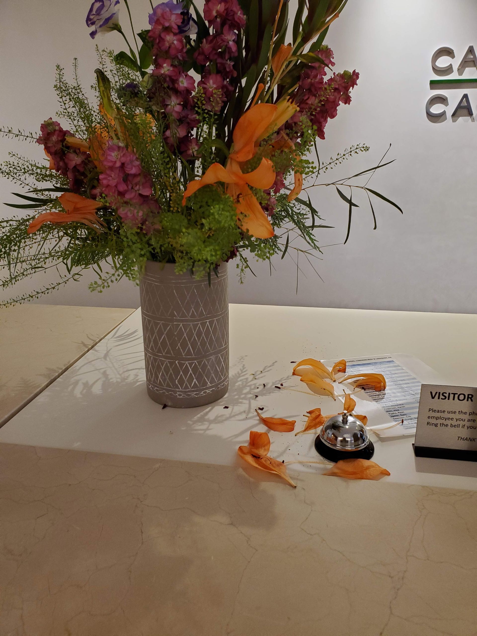 A vase of flowers sits on a table next to a visitor sign.