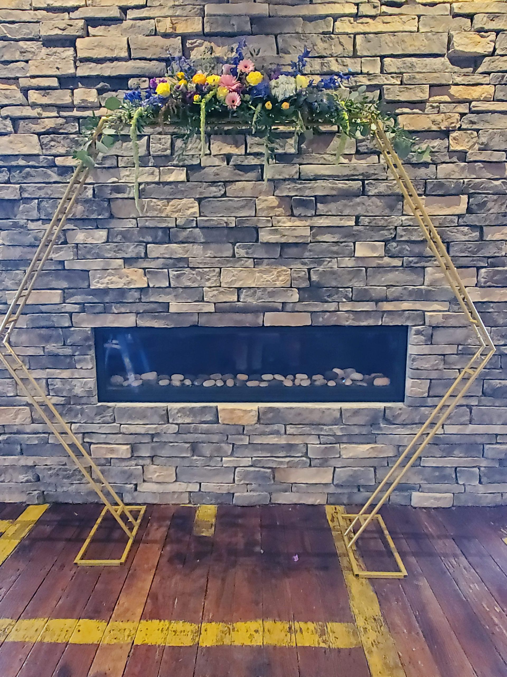 A fireplace with flowers on top of it in front of a brick wall.