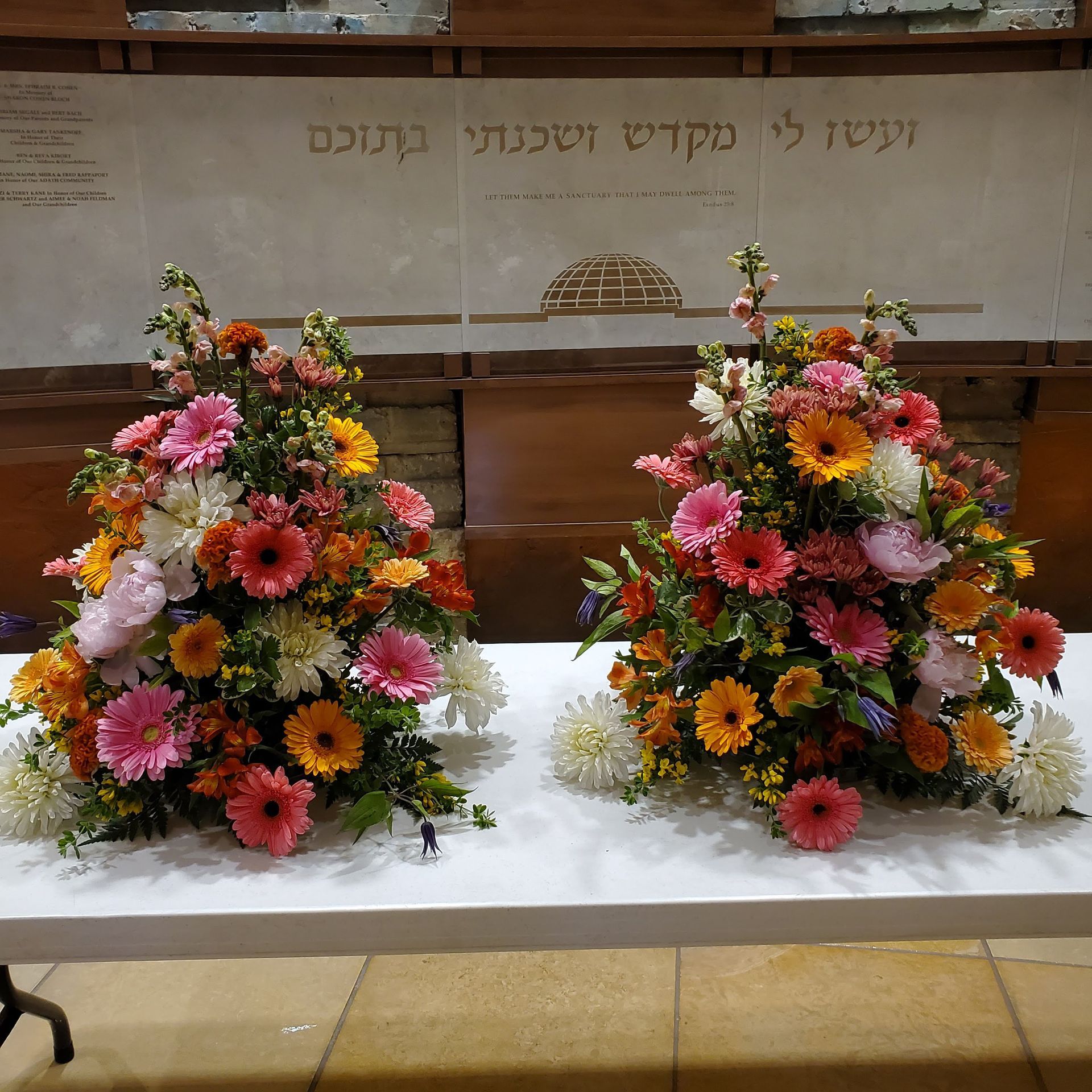 Two bouquets of flowers are on a table in front of a wall.