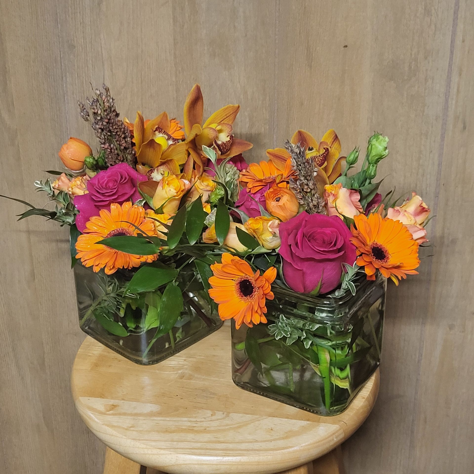 Two vases filled with flowers are sitting on a wooden stool.