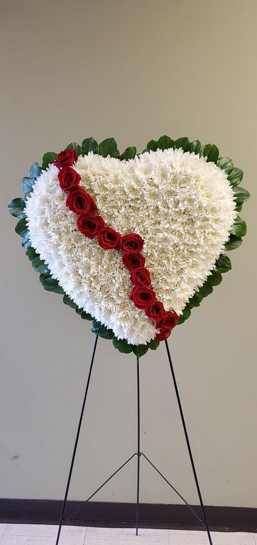 A broken heart made of white flowers and red roses on a stand.