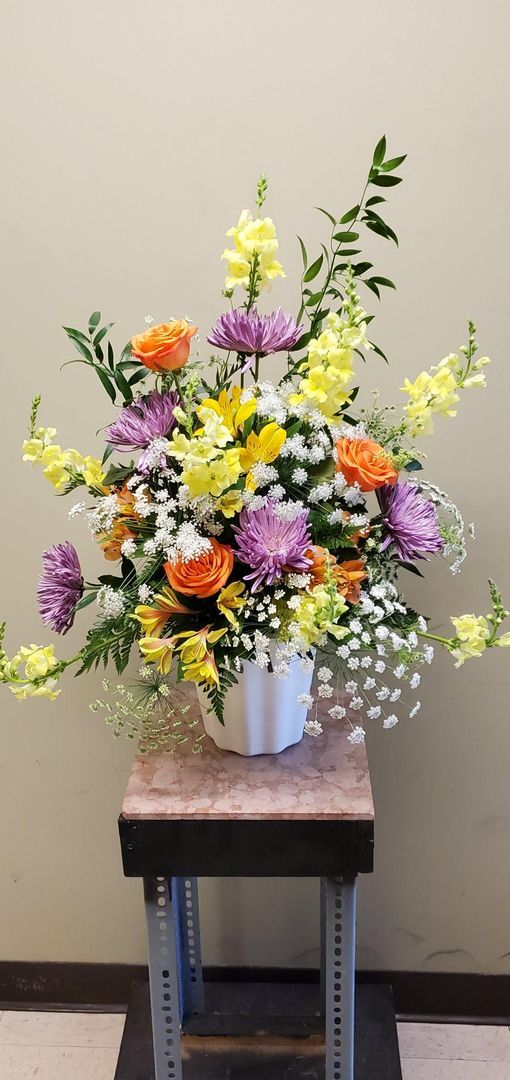 A vase filled with flowers is sitting on a stool.