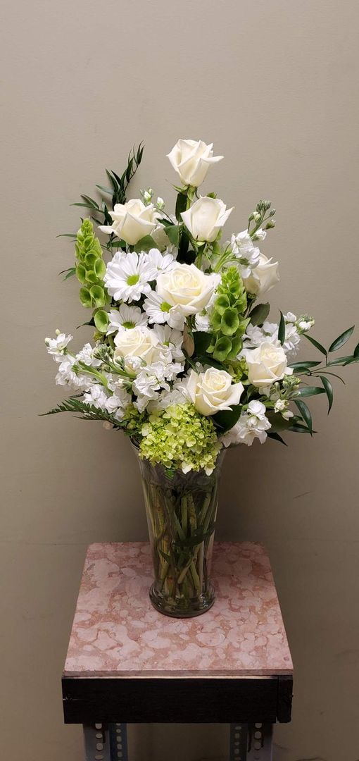 A vase filled with white flowers and greenery is sitting on a table.