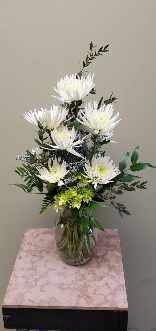 A vase filled with white flowers and greenery is sitting on a table.