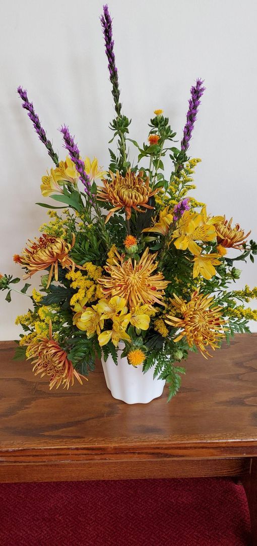 A vase filled with yellow and purple flowers is sitting on a wooden table.