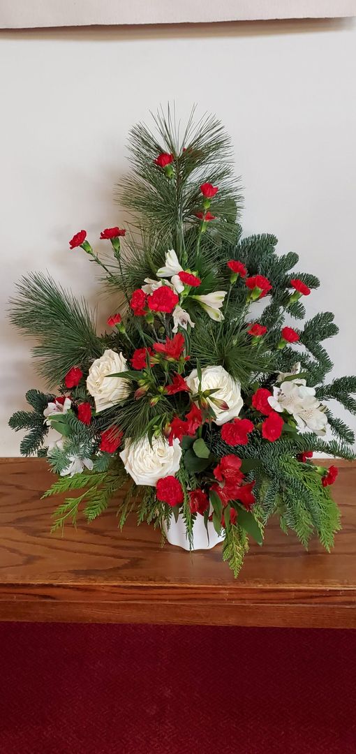 A vase filled with red and white flowers and pine branches on a wooden table.