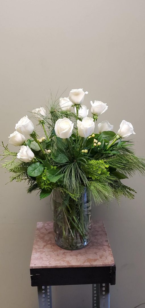 A vase filled with white roses and greenery is sitting on a table.