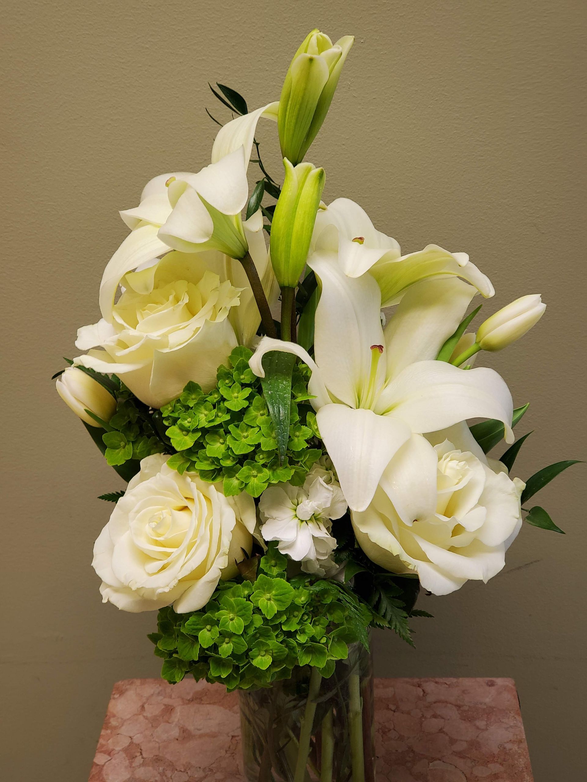 A vase filled with white flowers and greenery is sitting on a table.