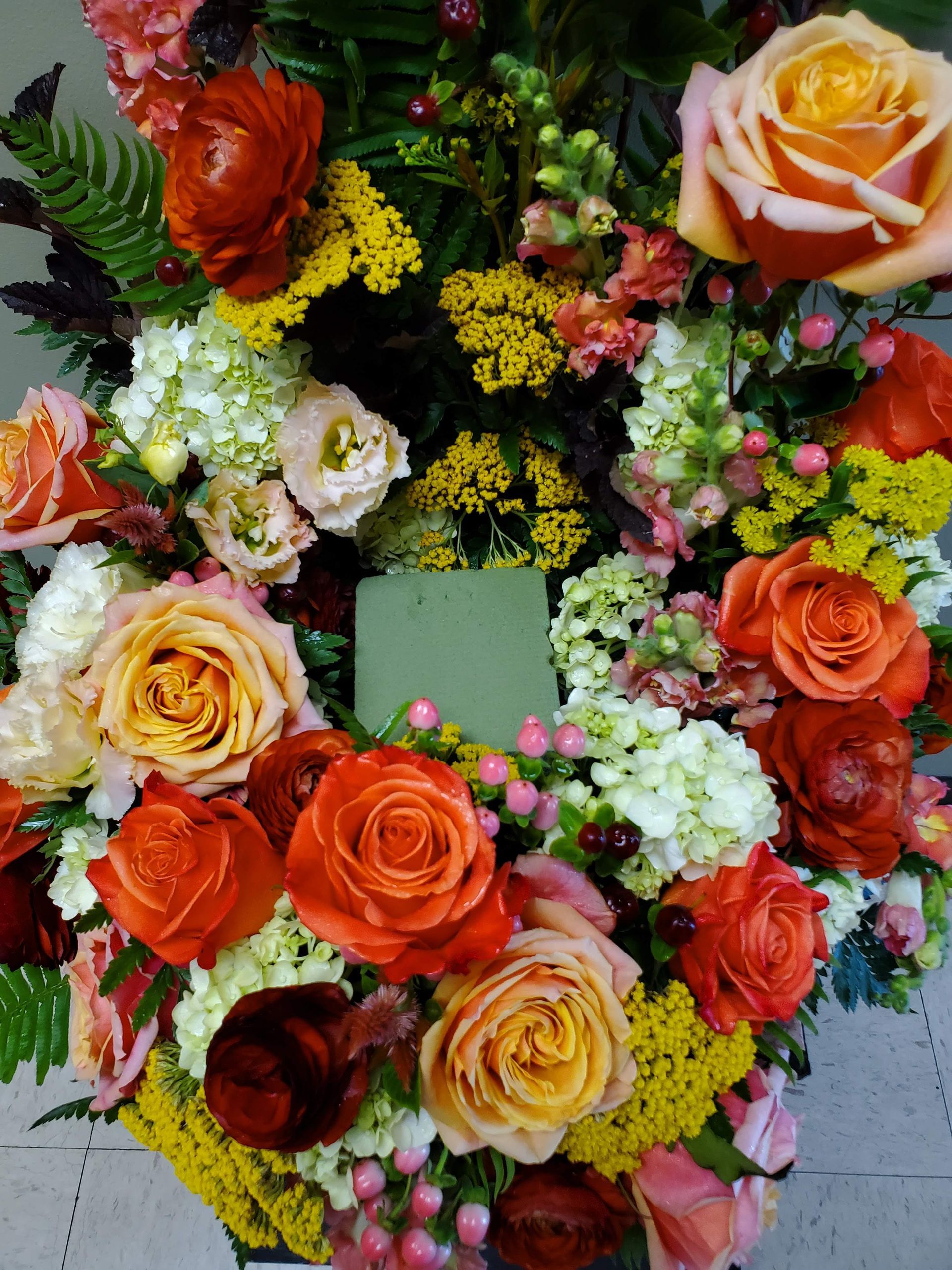 A wreath of flowers with orange roses and yellow flowers.