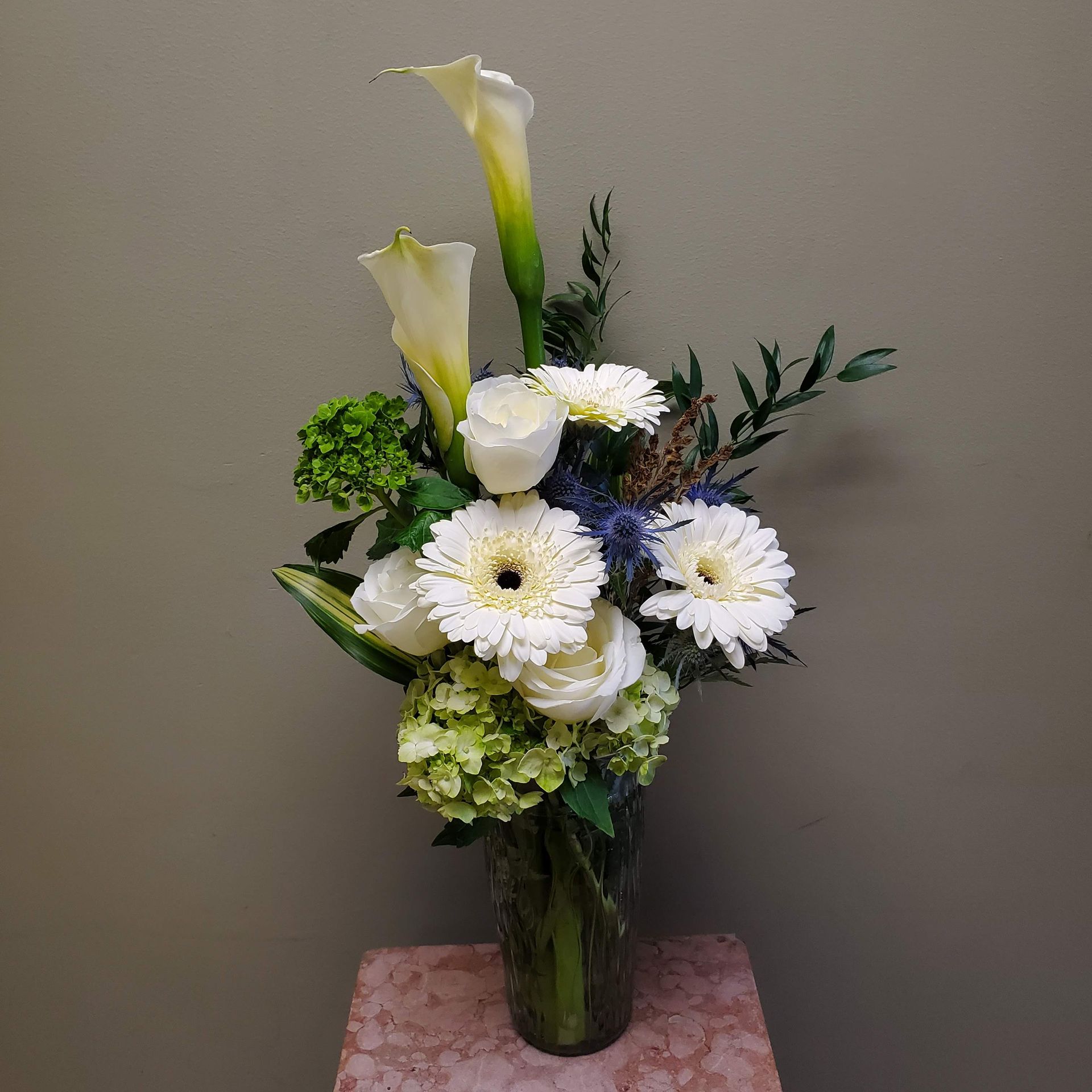 A vase filled with white flowers and greenery is sitting on a table.