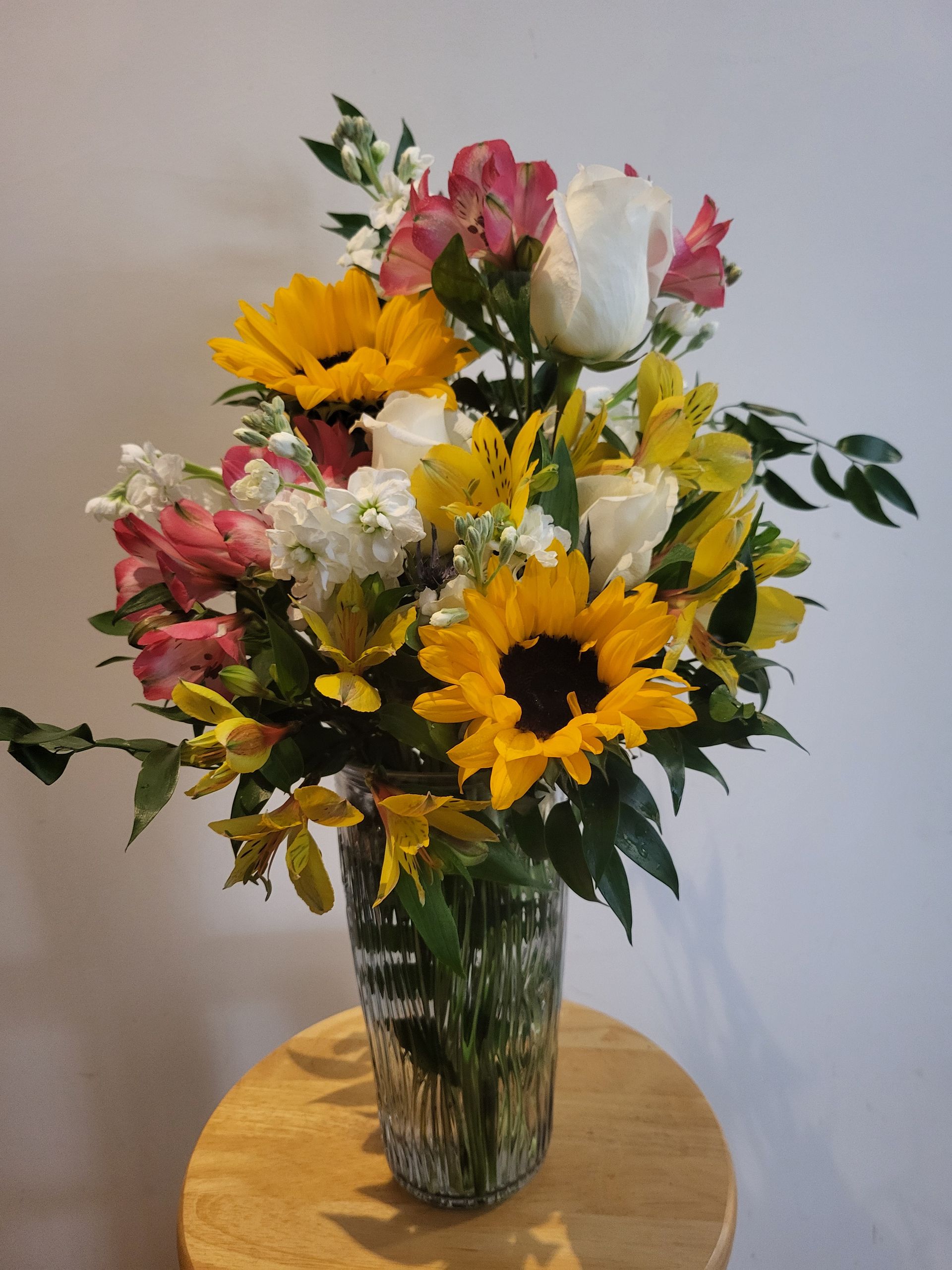 A vase filled with flowers is sitting on a wooden stool.