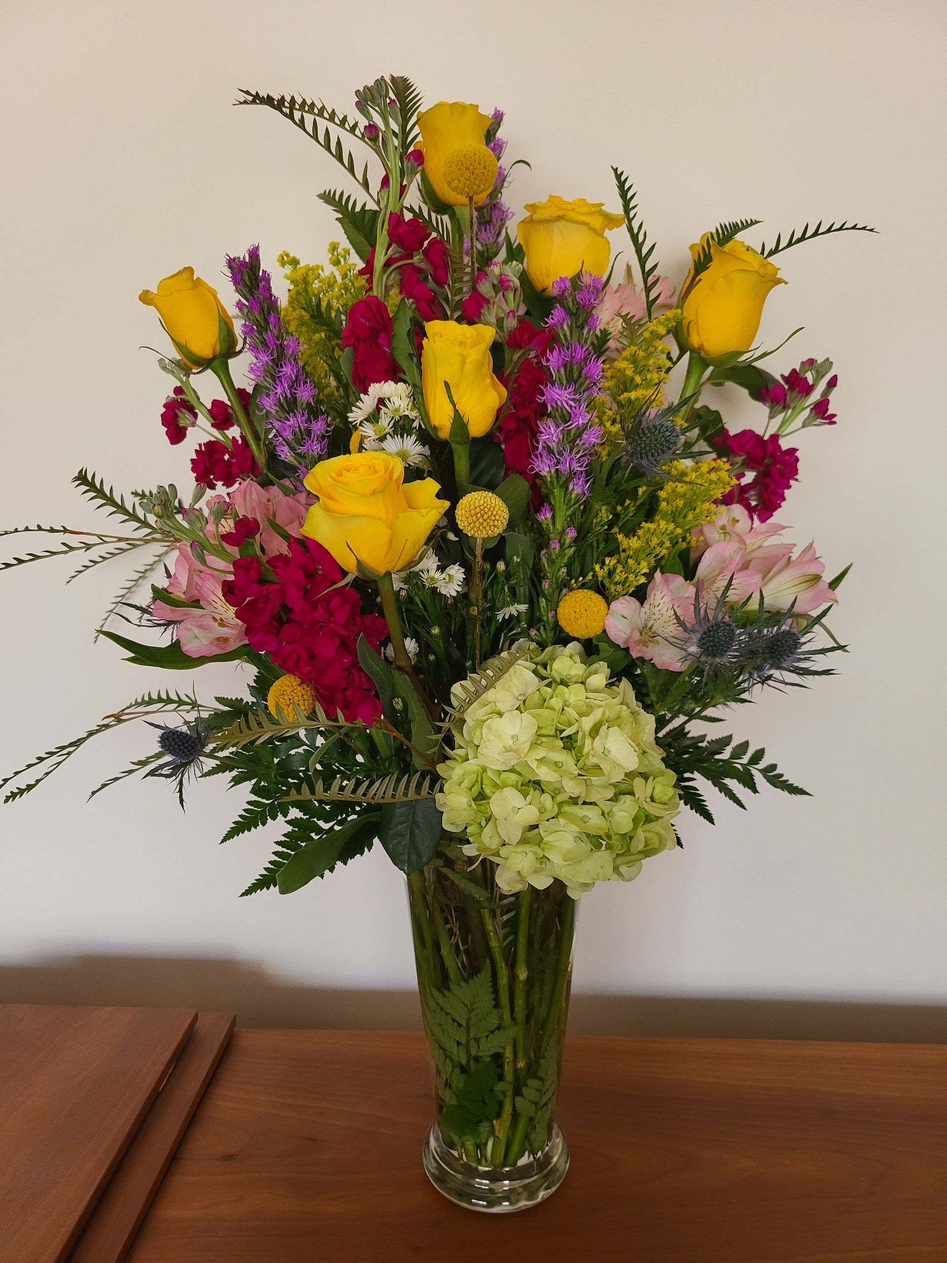A vase filled with colorful flowers including yellow roses.