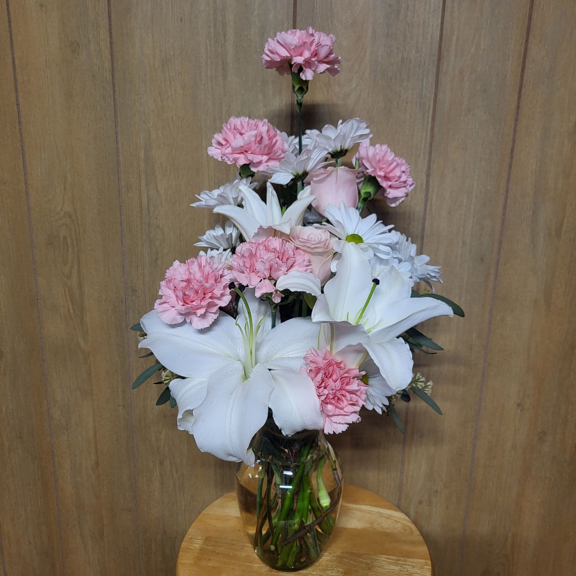 A vase filled with pink and white flowers is sitting on a wooden stool.