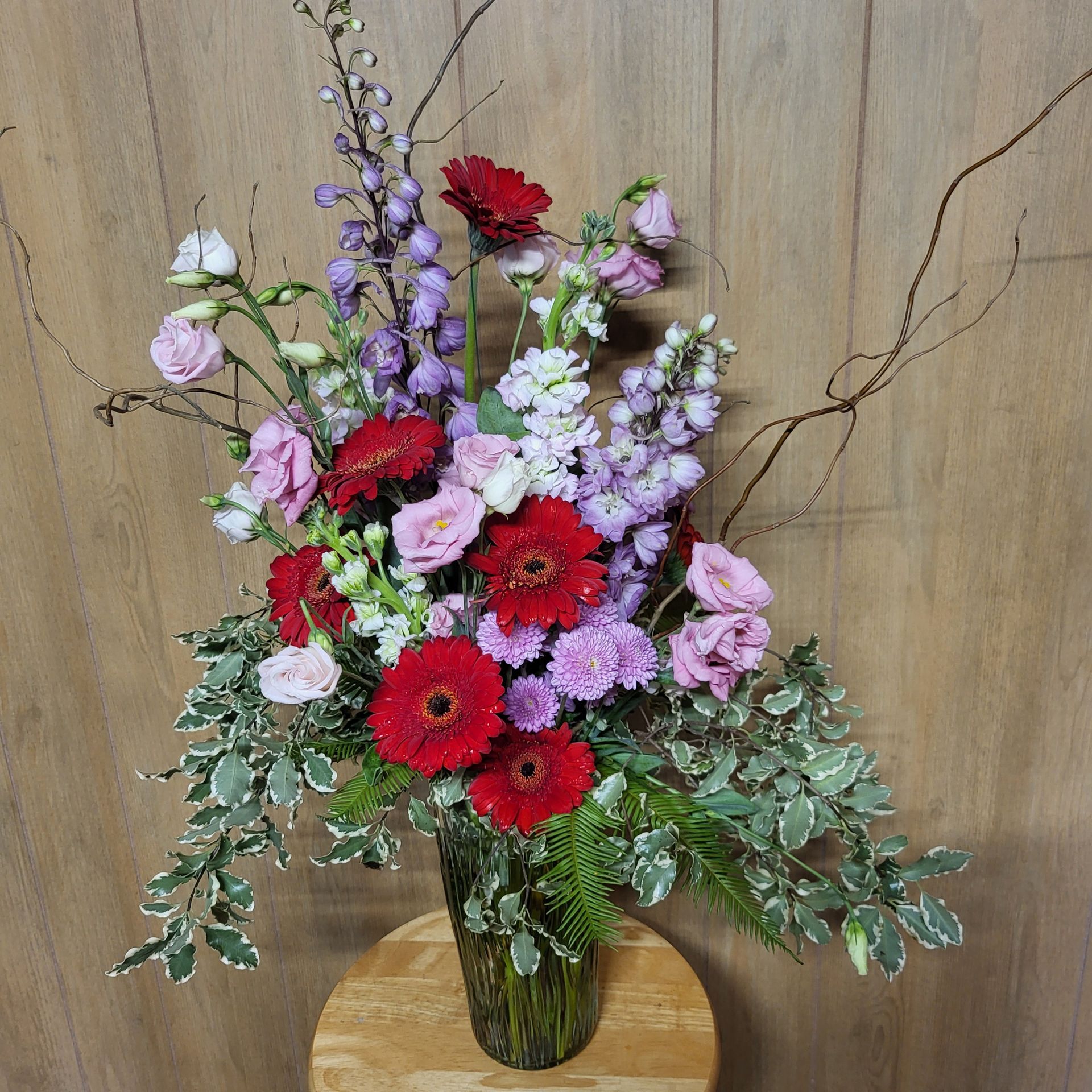 A vase filled with red and purple flowers is sitting on a wooden stool.