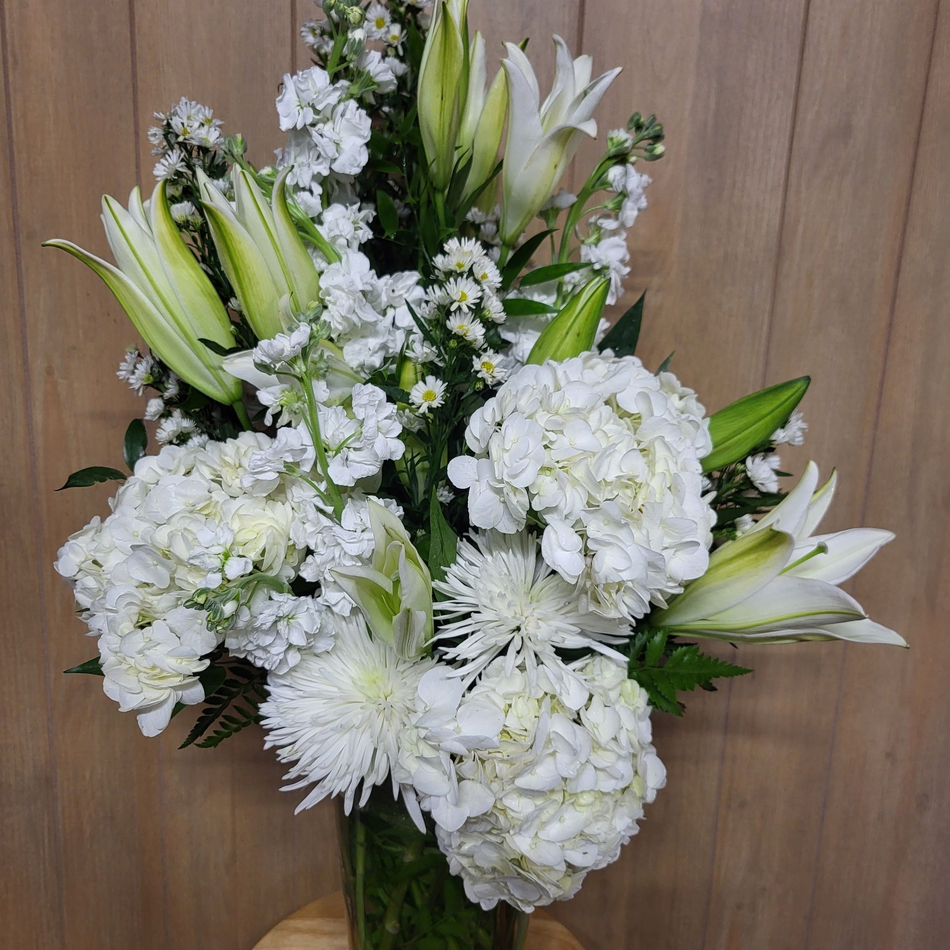 A vase filled with white flowers is sitting on a wooden table.