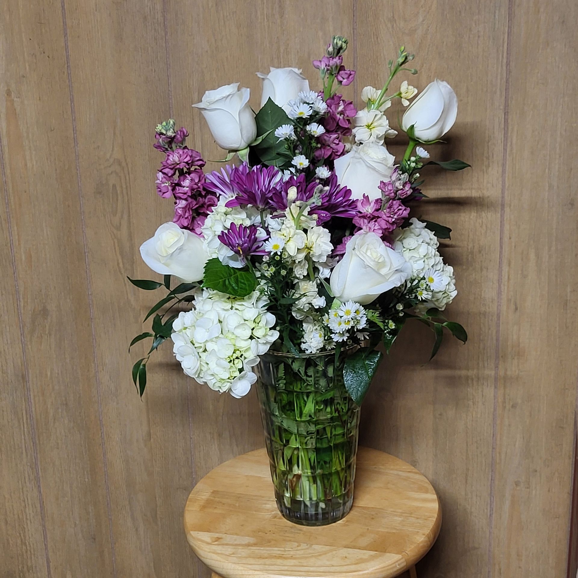 A vase filled with purple and white flowers is sitting on a wooden stool.