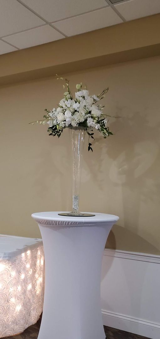 A tall vase filled with white flowers is sitting on top of a white table.