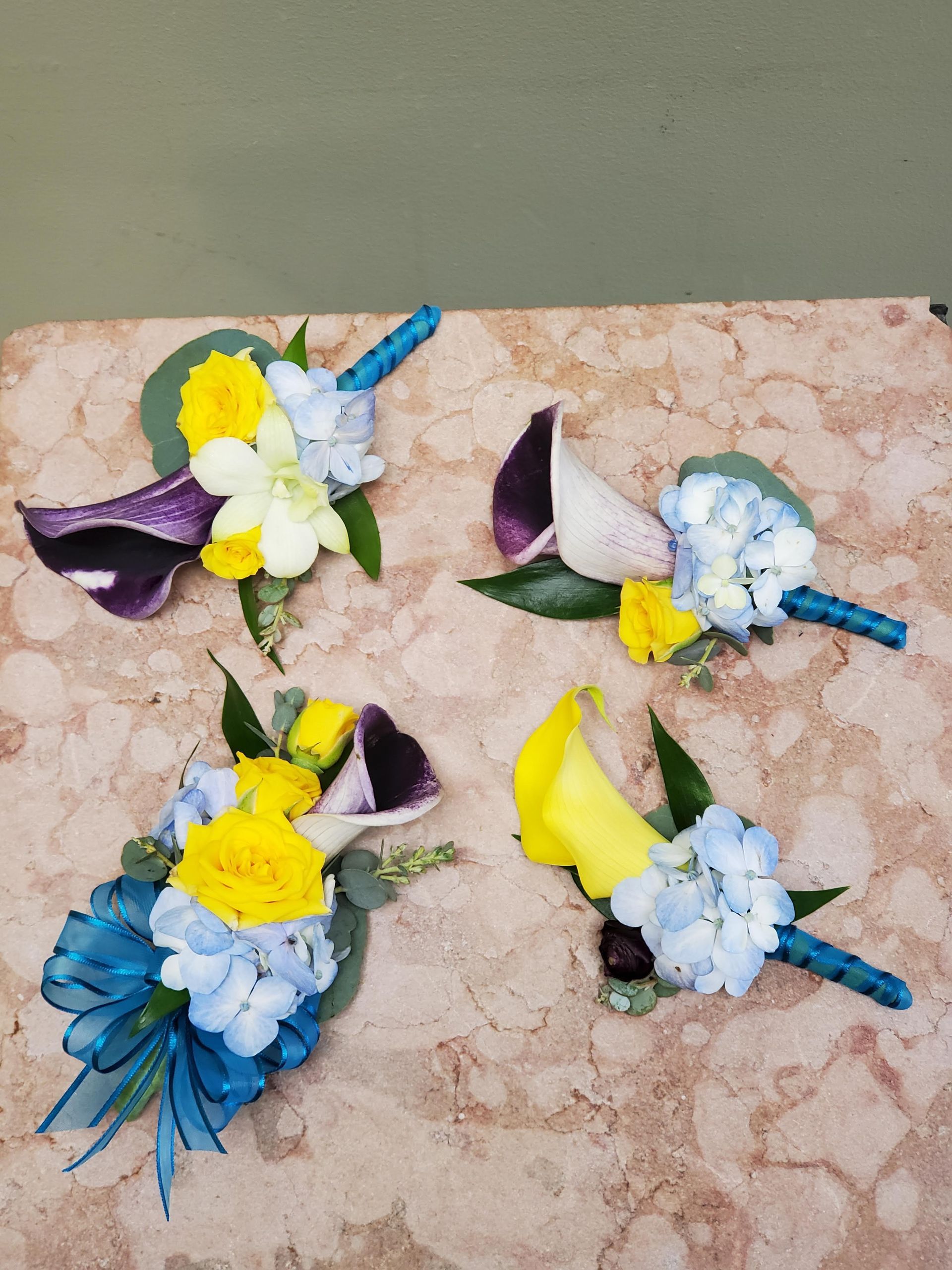 Four boutonnieres with yellow and blue flowers on a table.