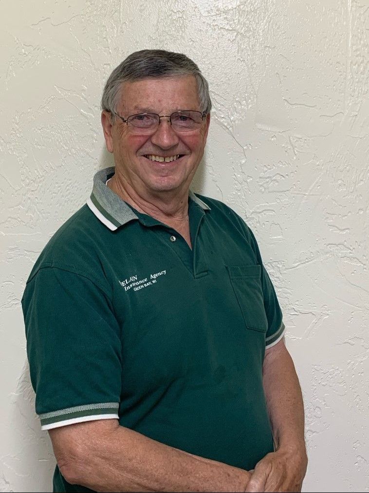 Man wearing glasses and a green polo shirt smiles in front of a neutral wall.