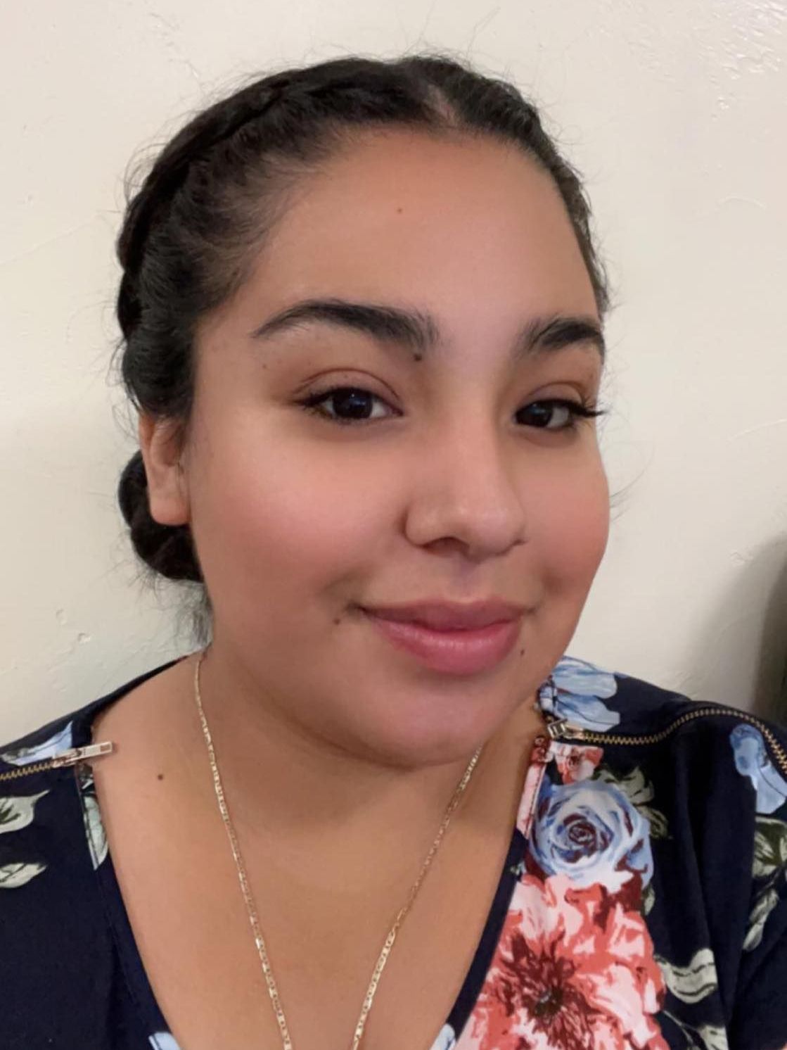 Woman with dark hair in a braid, smiling, wearing a floral top, against a neutral background.