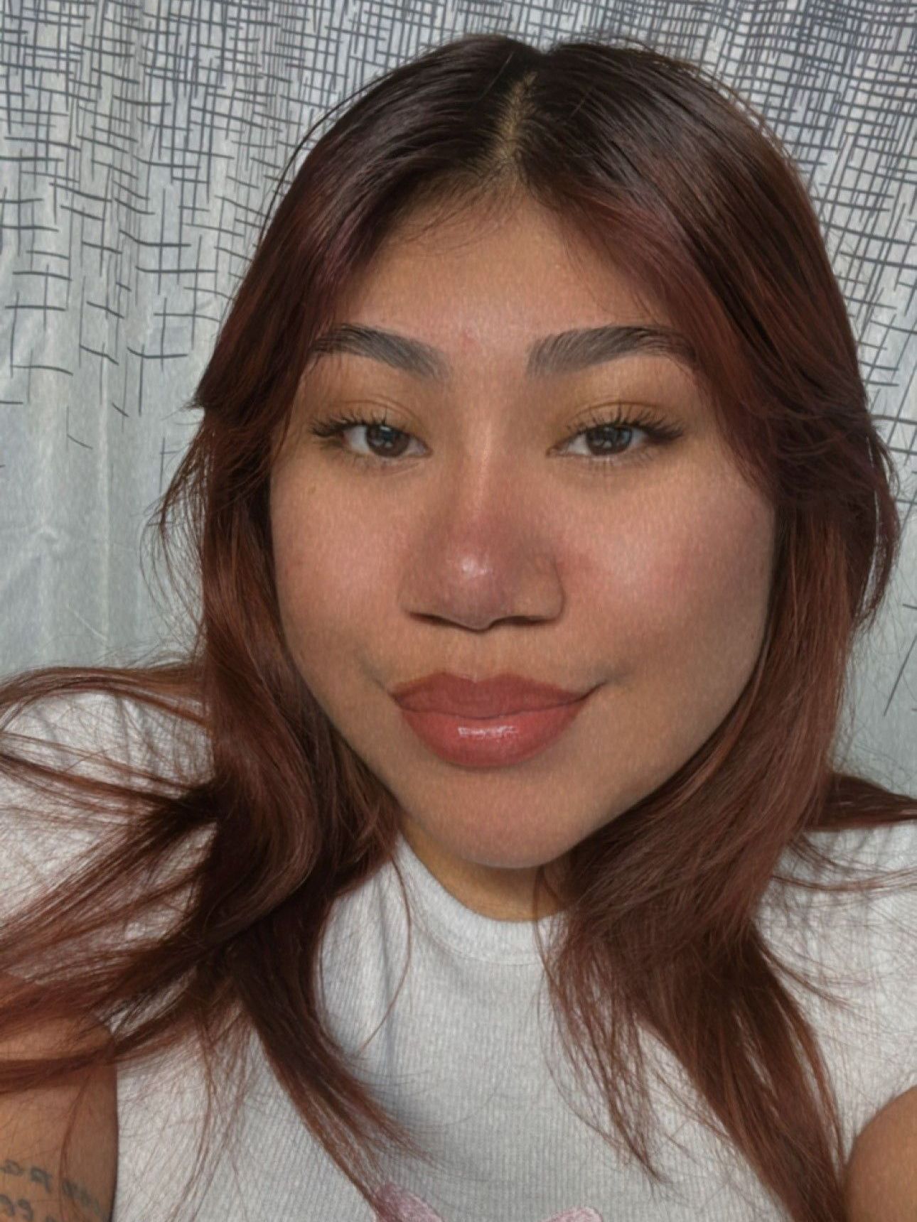 Woman with brown hair and light makeup smiling at the camera. She's wearing a white shirt against a patterned backdrop.
