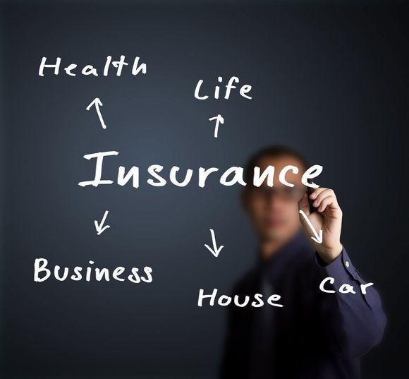Person writing insurance-related words: Health, Life, Business, House, and Car, on a dark background.